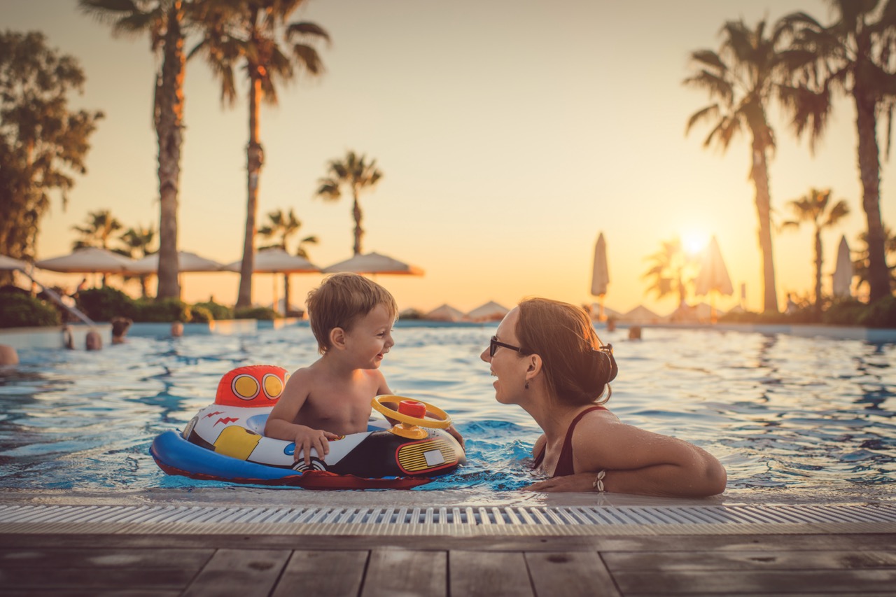A parent and toddler playing together in a hotel pool at sunset