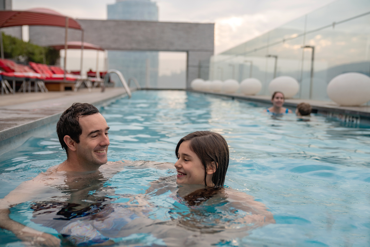 Two pairs swimming in a hotel rooftop pool, one of which is a private lesson